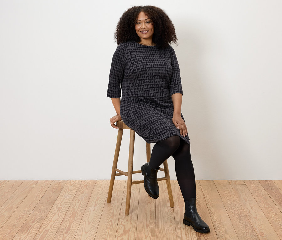 Frau sitzt auf einem Hocker und trägt ein Jerseykleid mit Hahnentritt-Jacquard.