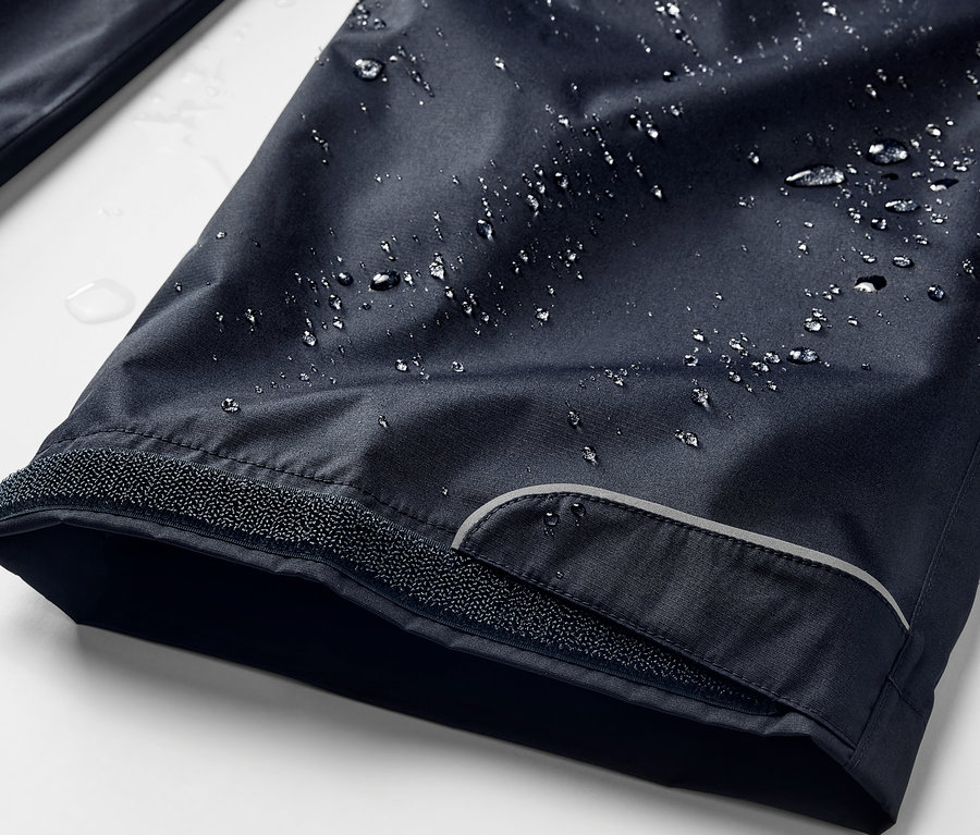 Detailaufnahme einer marineblauen Regenhose mit Wassertropfen.