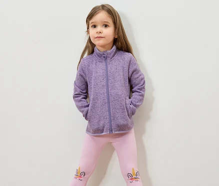 Mädchen mit braunen Haaren, lila Fleecejacke und rosa Leggings mit Einhornmotiv.