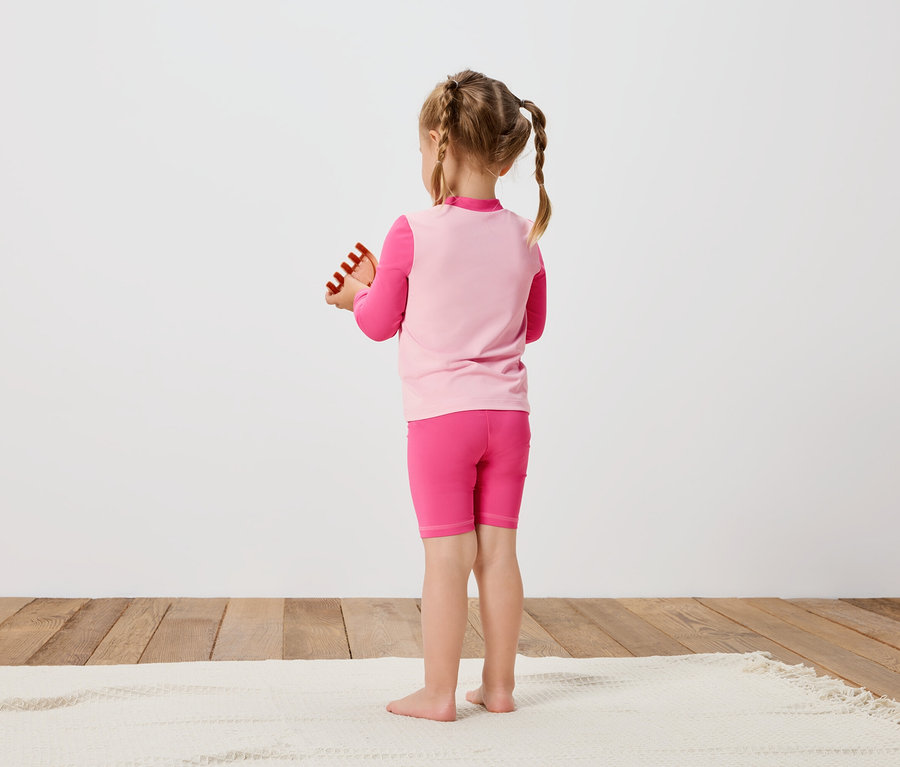 Mädchen von hinten in pinkfarbener Sportbekleidung, hält Spielzeug in den Händen.