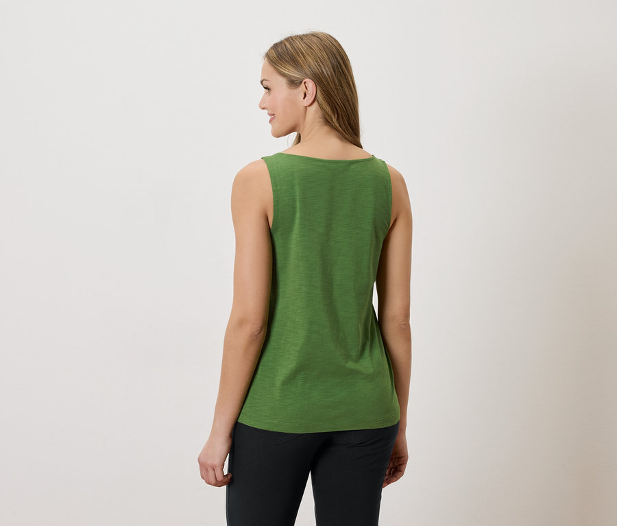 Frau von hinten, trägt ein grünes Tanktop und schwarze Hosen vor einem weißen Hintergrund.