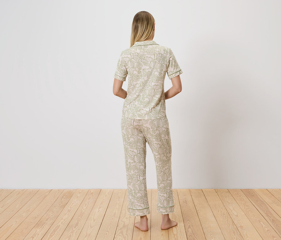 Rückansicht einer Frau mit blonden Haaren, die einen hellen Pyjama mit grünem Blumenmuster trägt.
