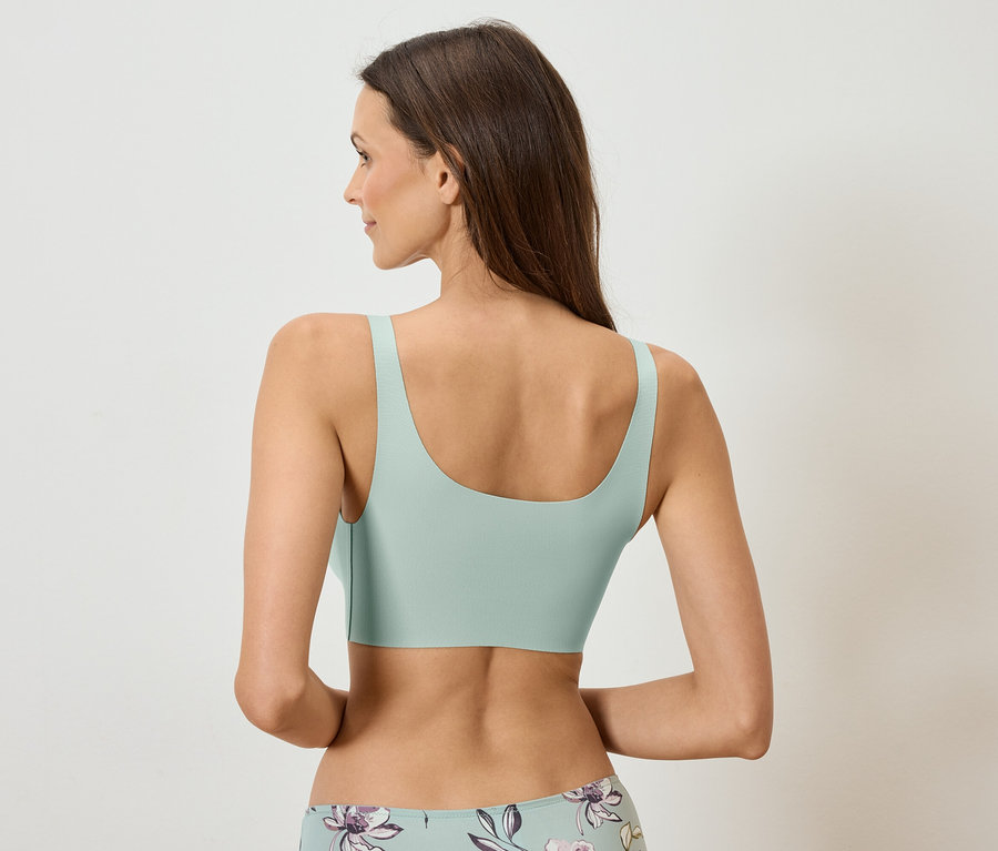 Rückansicht einer Frau mit langen braunen Haaren, die einen mintgrünen BH und Unterwäsche mit Blumenmuster trägt.