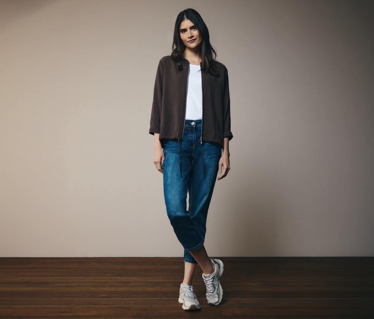 Frau mit weißem T-Shirt, Jeans und braunem CECIL Blouson. Sie steht vor einer Wand.