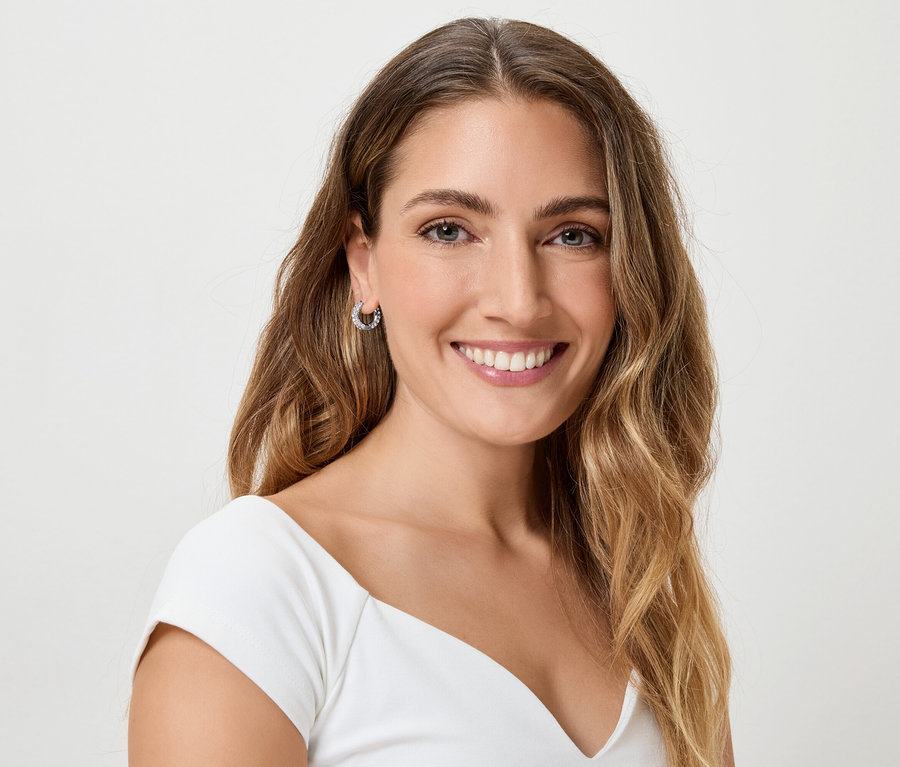 Frau mit langen, gewellten, braunen Haaren und Ohrringen, die in die Kamera lächelt.