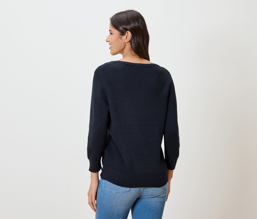 Frau von hinten, trägt dunkelblauen Feinstrickpullover und Jeans.