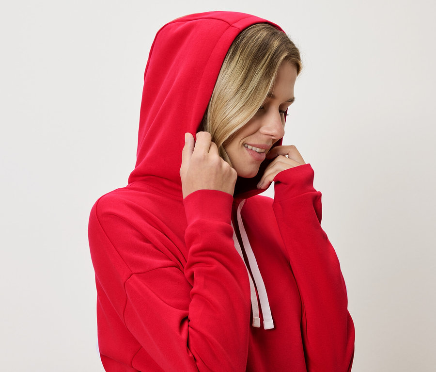 Frau mit blonden Haaren trägt einen roten Kapuzenpullover und hält die Kapuze fest.