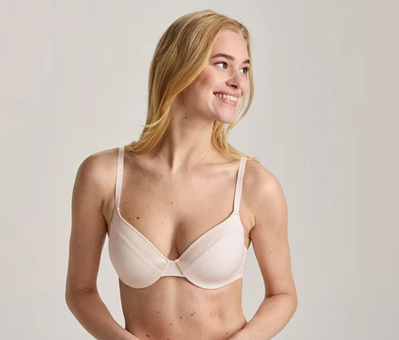 Blonde Frau trägt einen hellrosa BH, lächelt und blickt nach rechts.