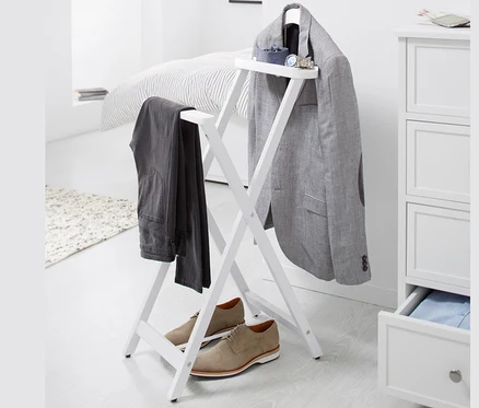 Auf einem weißen Hintergrund steht ein stummer Diener, an dem ein grauer Blazer und eine Hose hängen, darunter stehen braune Schuhe.