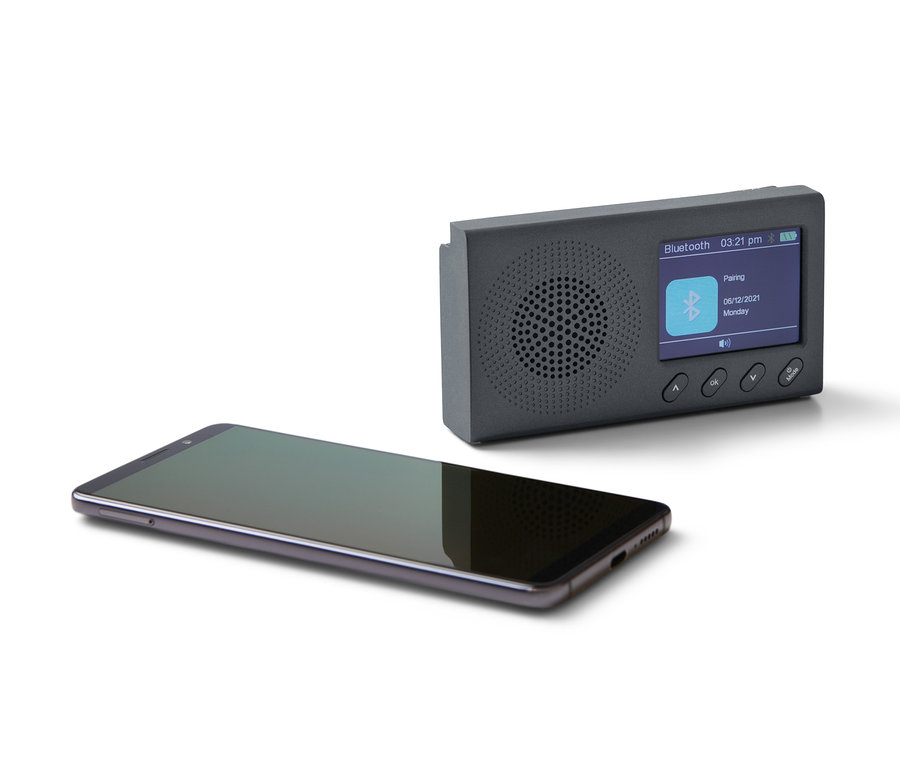 Ein schwarzes, tragbares DAB/FM-Radio mit Bluetooth und ein schwarzes Smartphone liegen auf einem weißen Hintergrund.