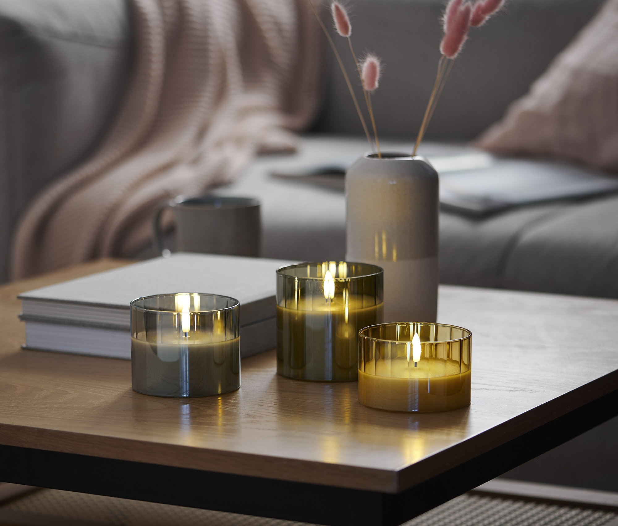 Drei LED-Echtwachskerzen im Glas stehen auf einem Tisch im Wohnzimmer.