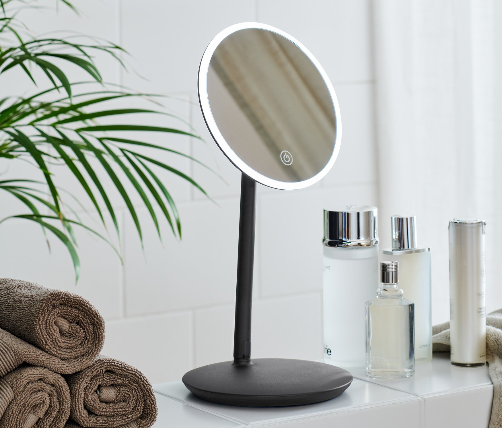 Ein Badezimmer mit einem beleuchteten LED-Kosmetikspiegel, Kosmetika und einem Stapel Handtücher.