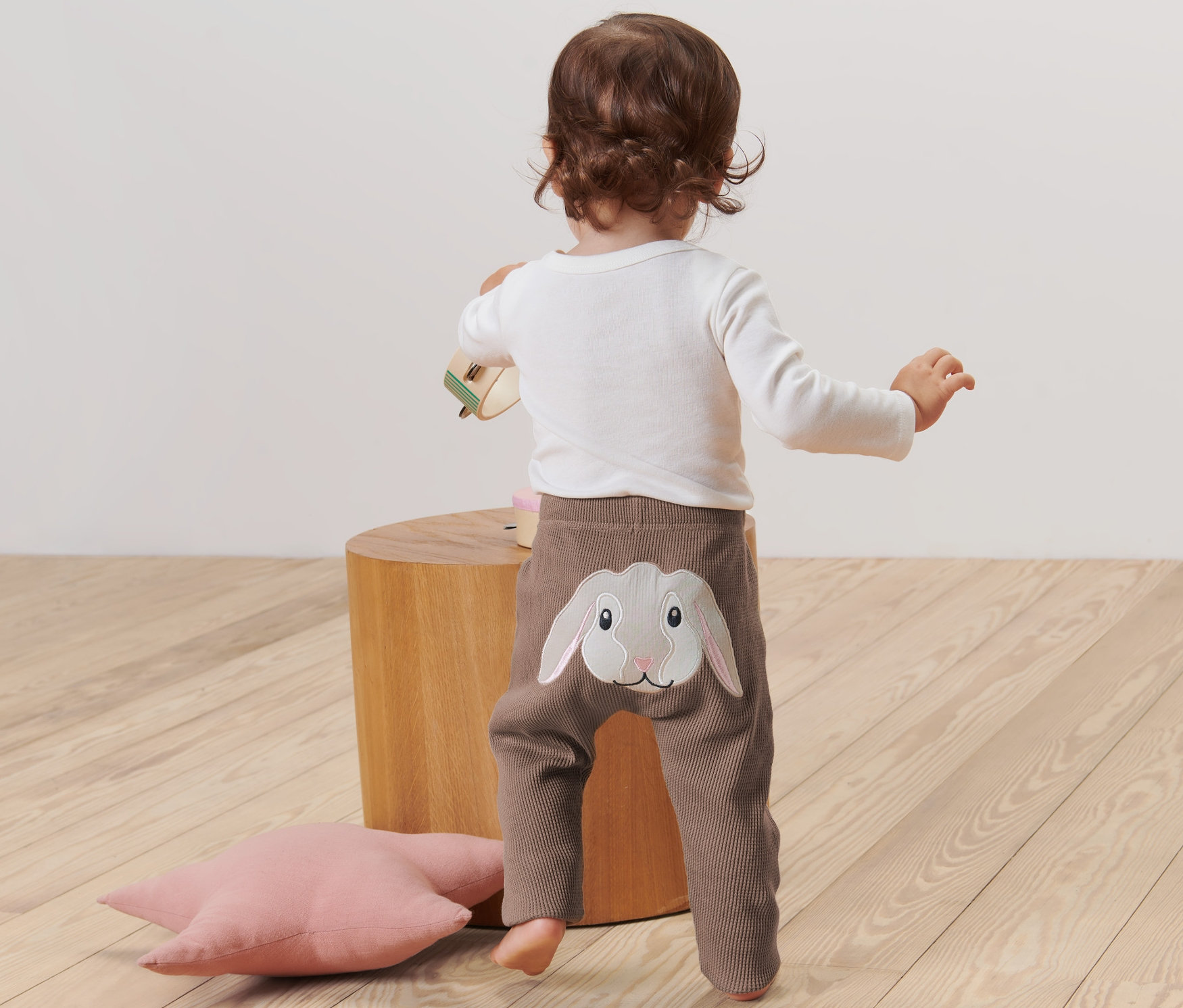 Kleinkind steht mit dem Rücken zur Kamera und trägt eine Babyhose mit Hasenapplikation.