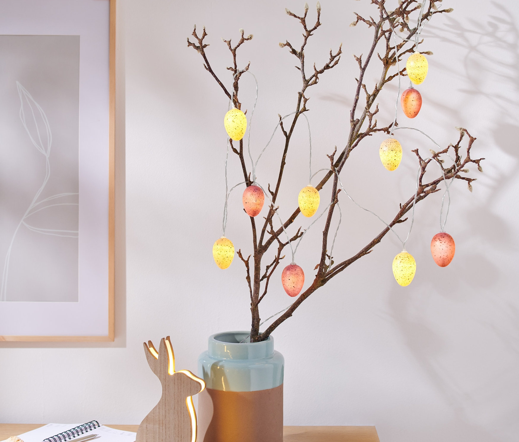 Zweige in Vase geschmückt mit LED-Lichterkette in Eiform.