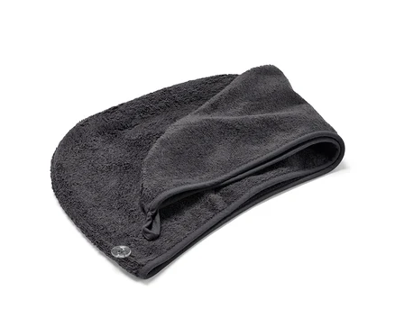 Ein anthrazitfarbenes Turban-Handtuch liegt gefaltet auf einem weißen Hintergrund.