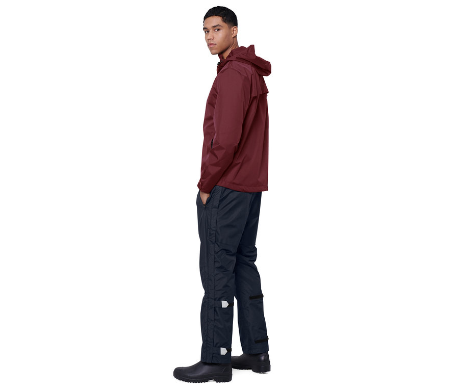 Mann posiert in einer burgunderroten Jacke und einer dunkelblauen Unisex-High-Tech-Regenhose.