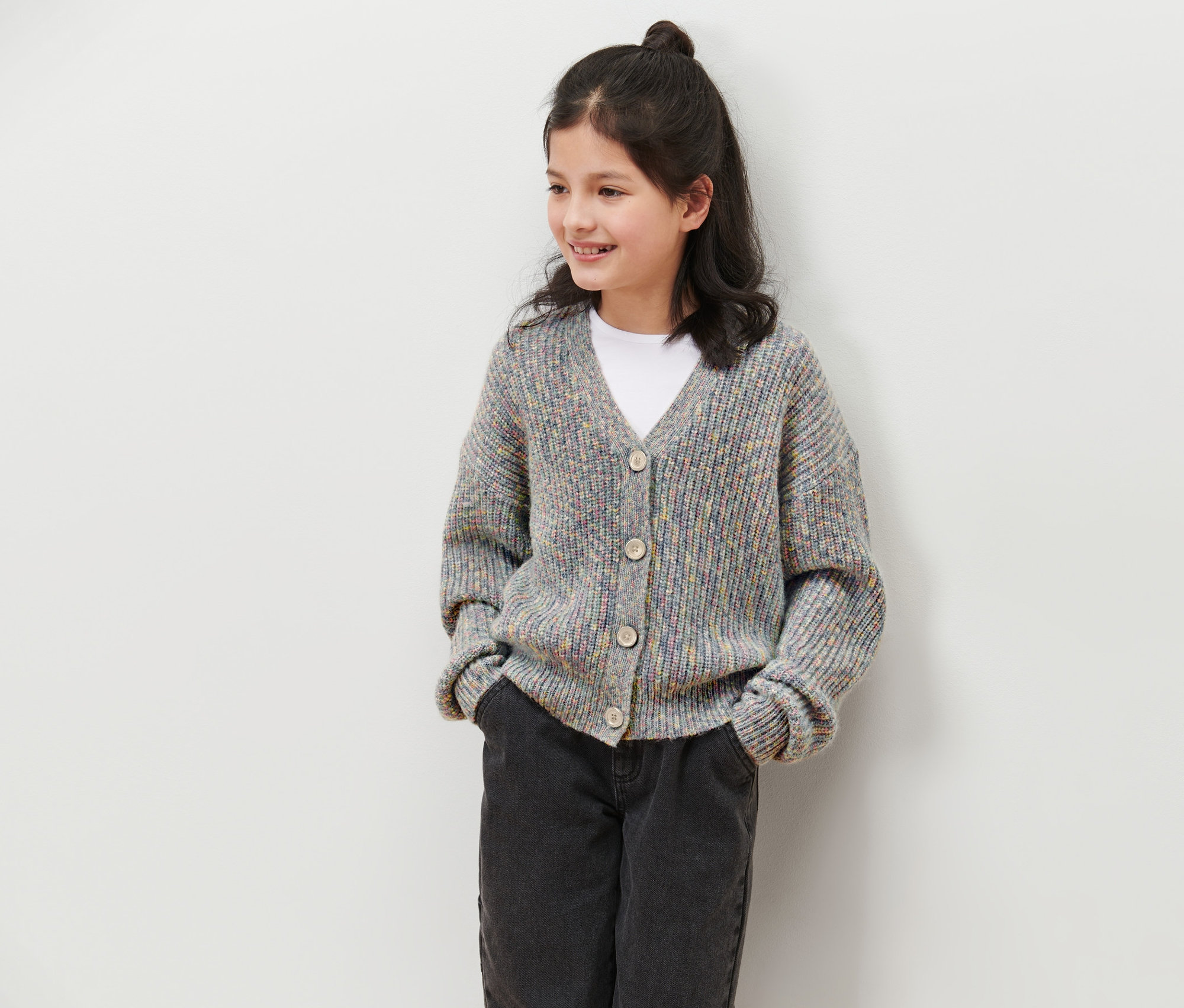 Mädchen trägt eine Kinder-Strickjacke mit Wolle, Jeans und T-Shirt.