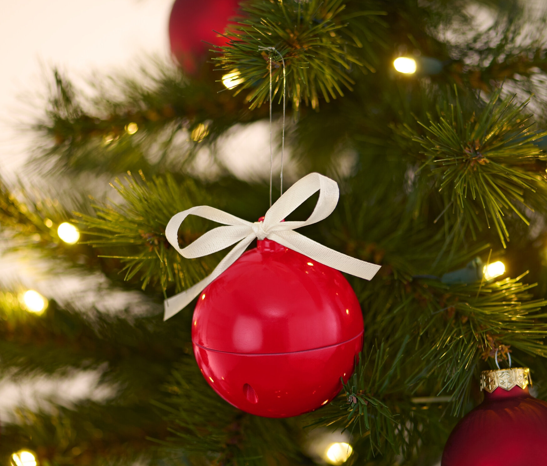 Eine rote singende Weihnachtskugel hängt an einem Weihnachtsbaum mit anderen roten Kugeln und Lichtern.