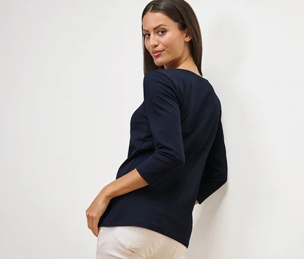 Frau blickt über die Schulter und trägt ein marineblaues Shirt mit 3/4-Arm.