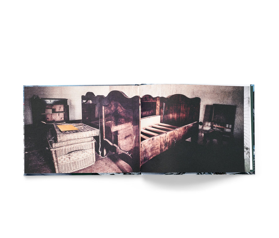 Aufgeschlagenes Buch zeigt ein altes Zimmer mit einem Holzbett, einer Kommode und Weidenkörben.