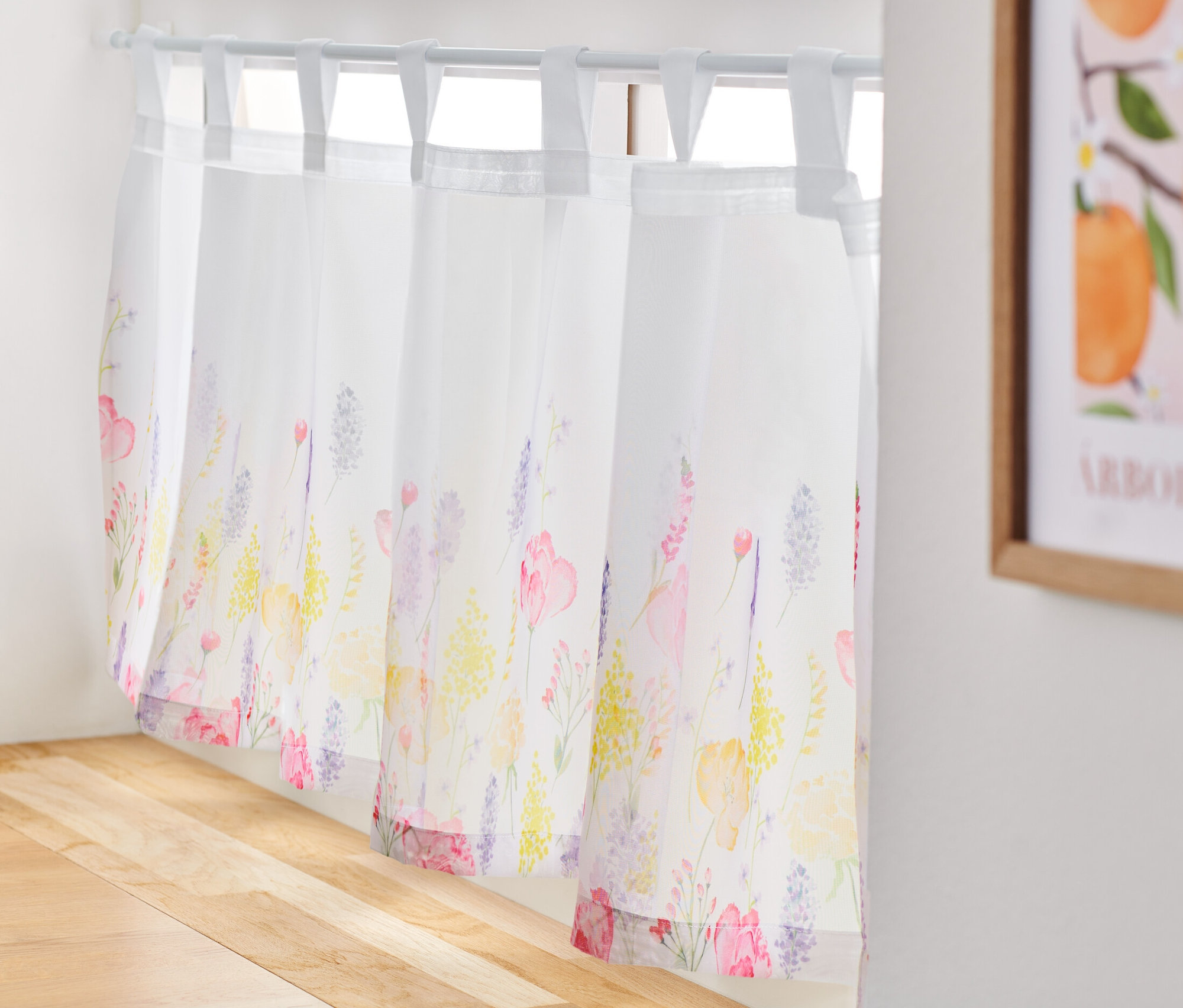 Eine bedruckte Bistrogardine hängt an einem Fenster.