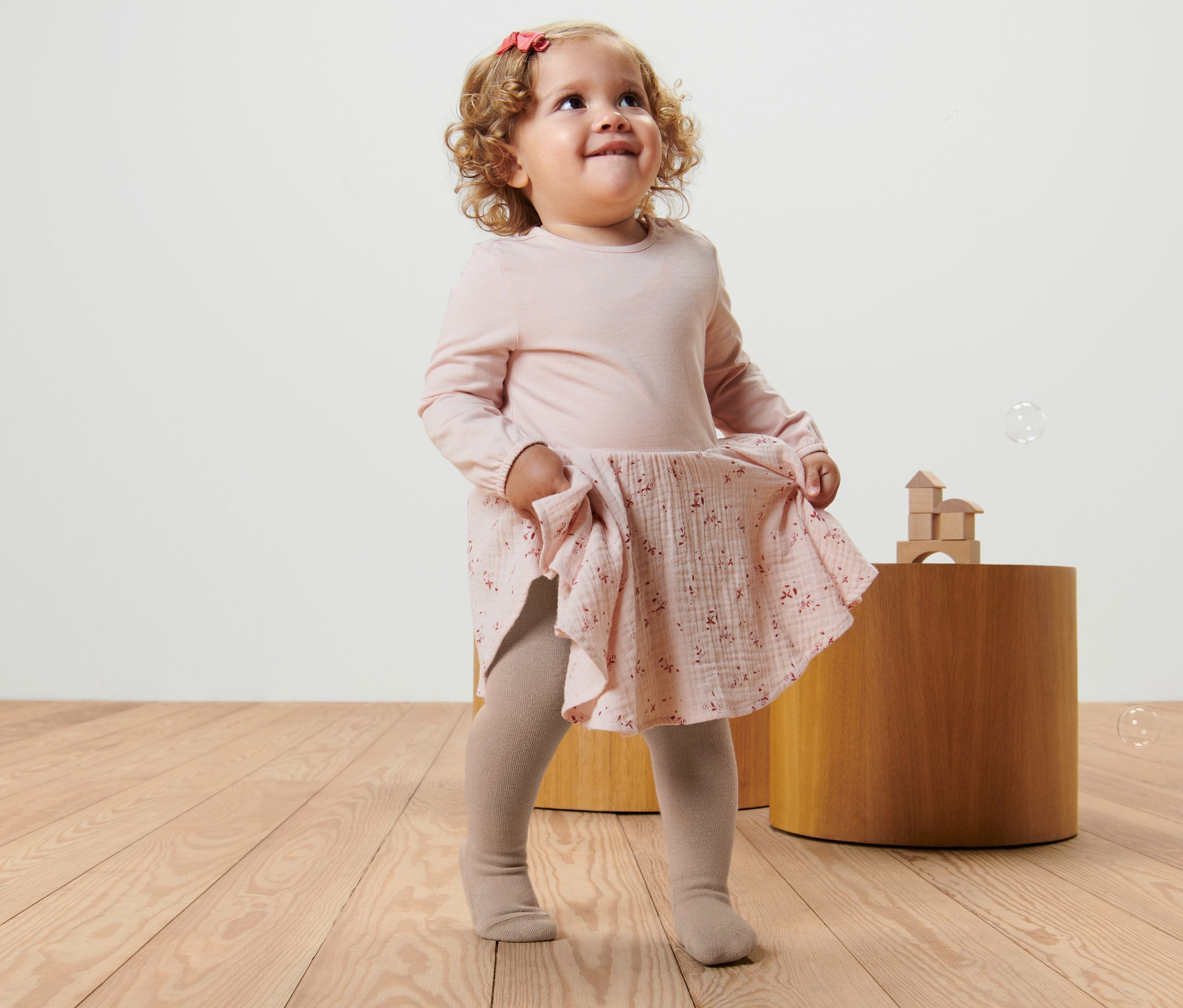 Kleines Mädchen in rosa Kleid und beigen Strumpfhosen (5 Kinder-Strumpfhosen) spielt mit Seifenblasen.