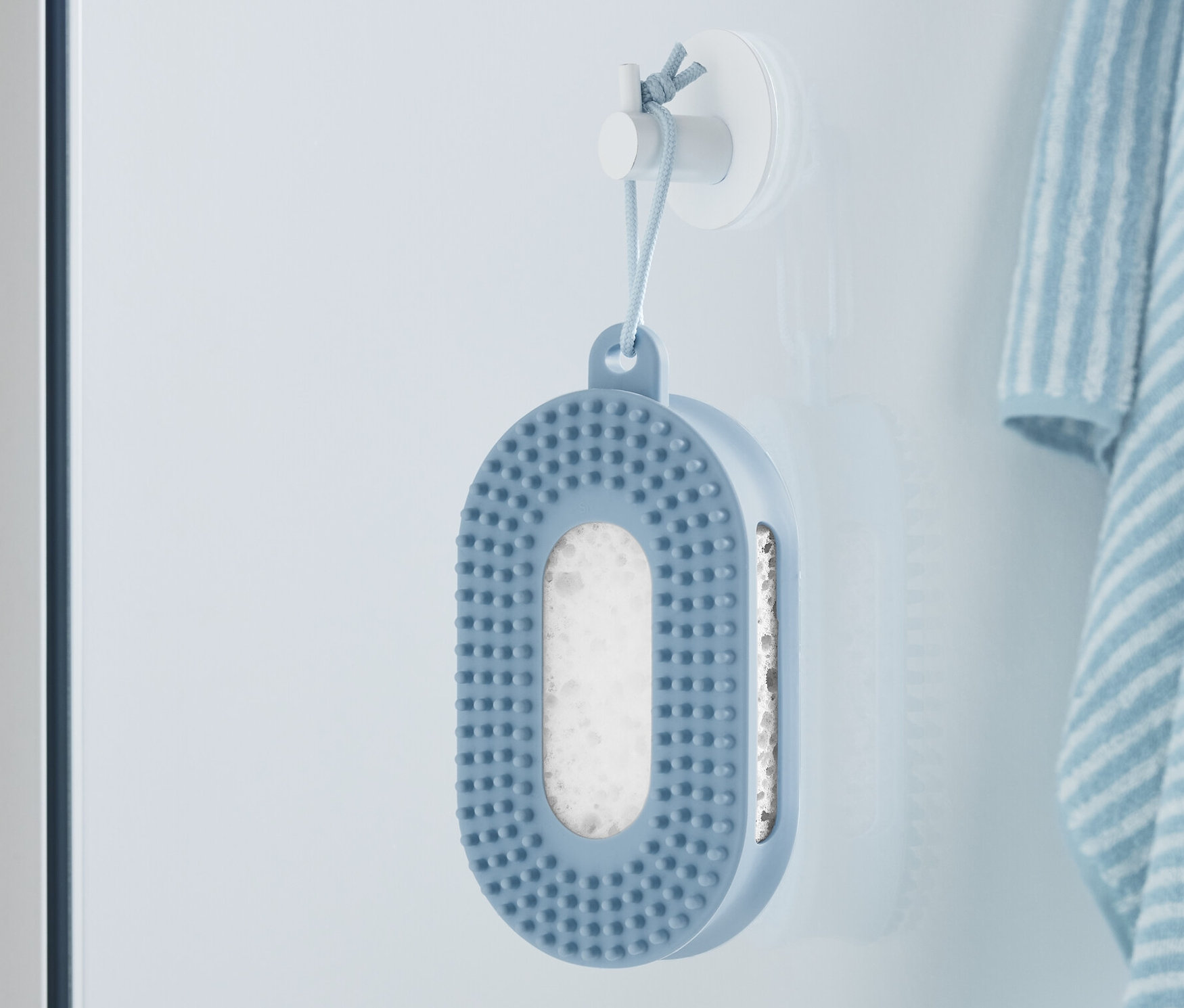 Blauer Duschschwamm hängt an der Wand neben einem gestreiften Handtuch.