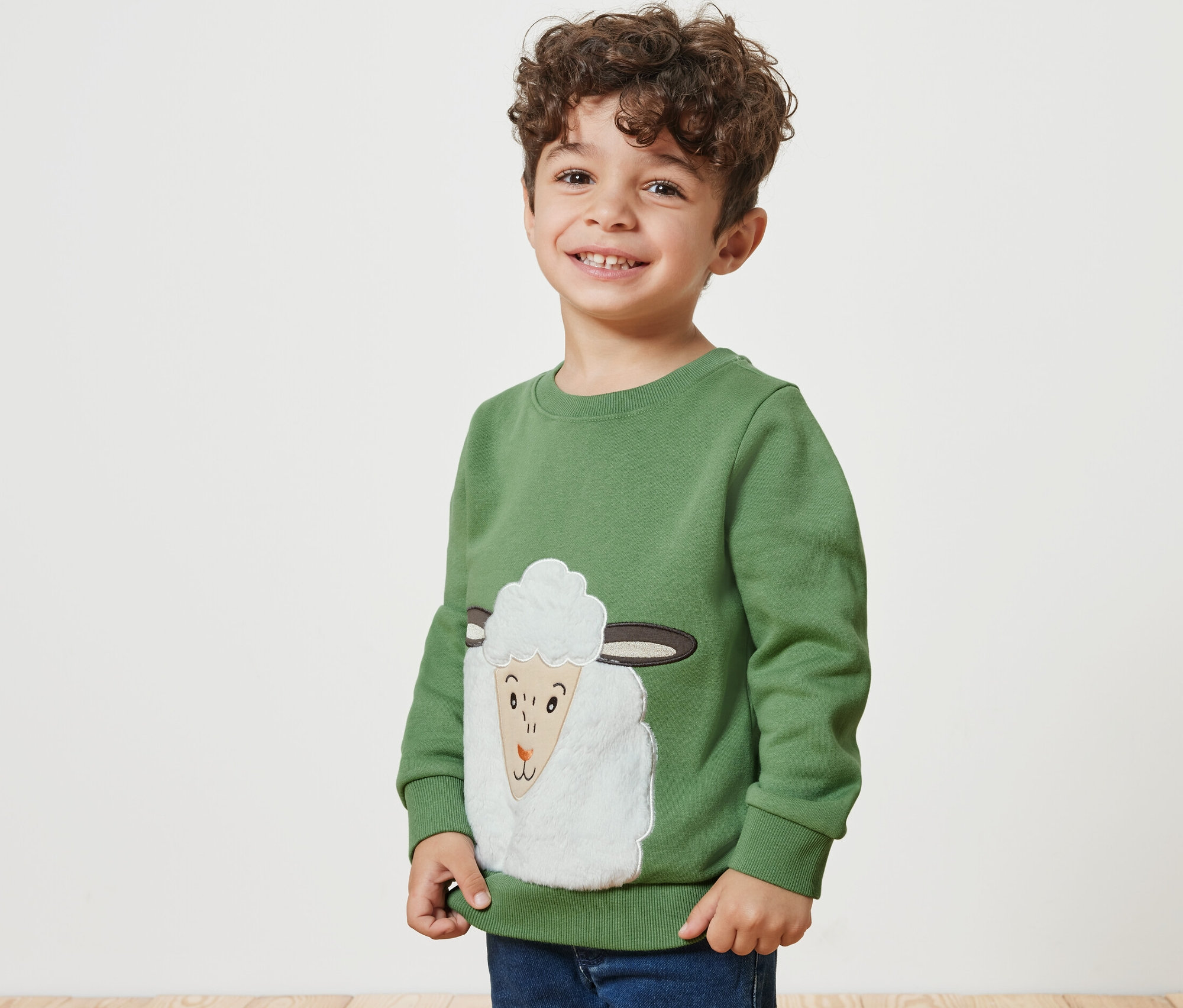 Lächelnder Junge trägt ein Kinder-Sweatshirt mit angerauter Innenseite und einem Schaf-Motiv.