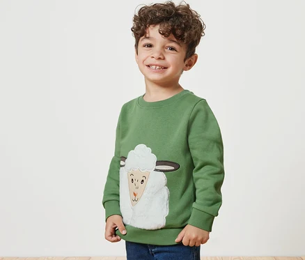 Lächelnder Junge trägt ein Kinder-Sweatshirt mit angerauter Innenseite und einem Schaf-Motiv.