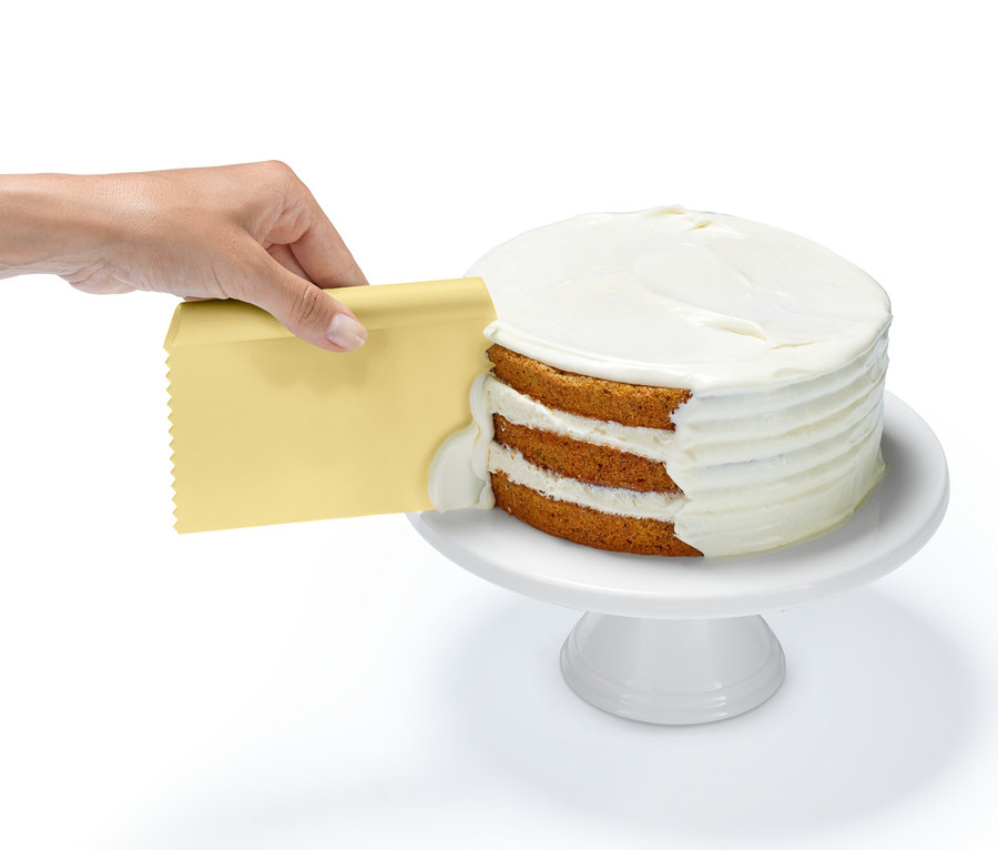 Eine Hand trägt mit einem gelben Schaber aus dem Profi-Backhelfer-Set Zuckerguss auf eine Torte auf.