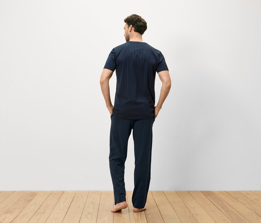 Mann von hinten in blau gestreiftem T-Shirt und Hose auf Holzboden.