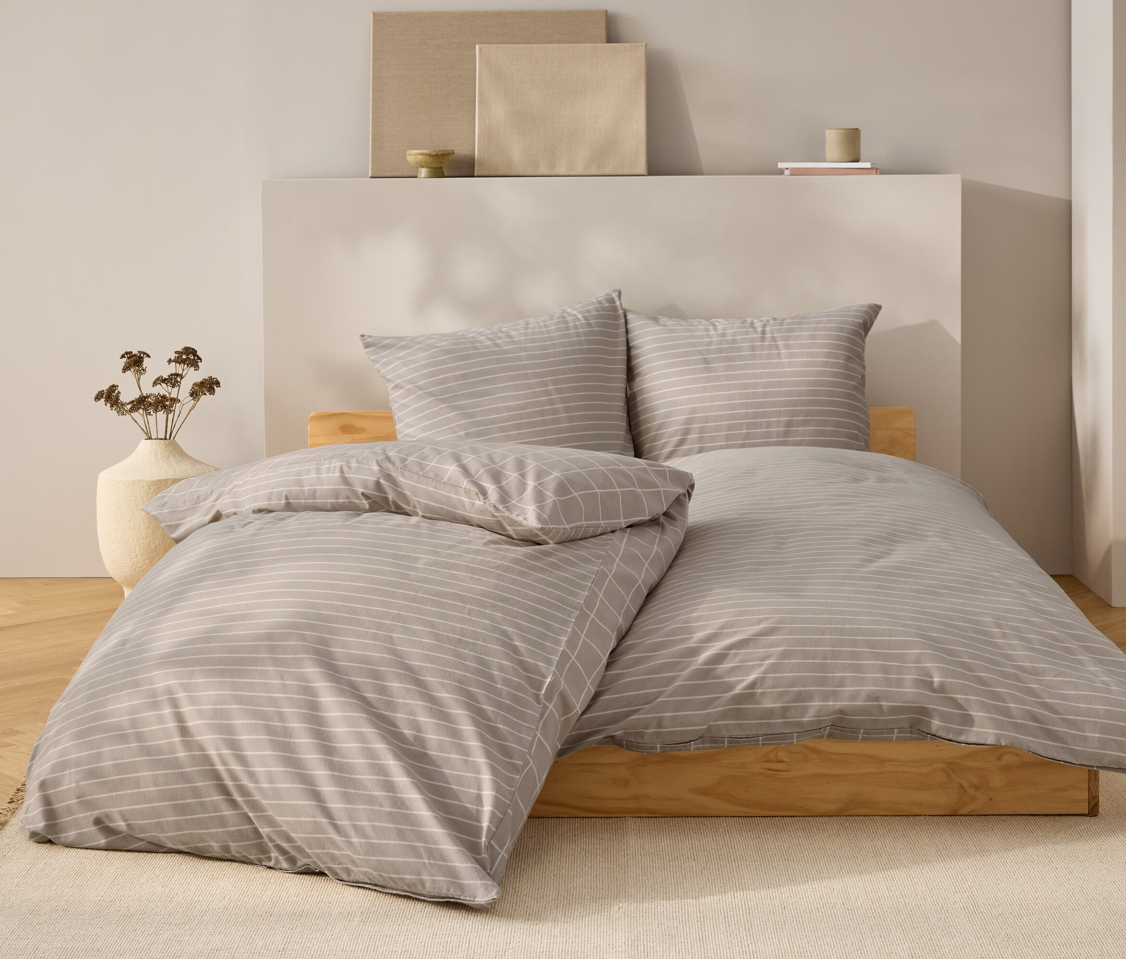 Bettwäsche mit grauen und weißen Streifen auf einem Bett aus Naturholz.