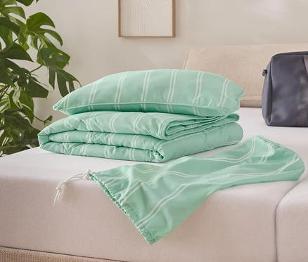 Auf einem Bett liegen eine gefaltete hellgrüne Steppdecke mit weißen Streifen, ein Kissen und eine Tasche.
