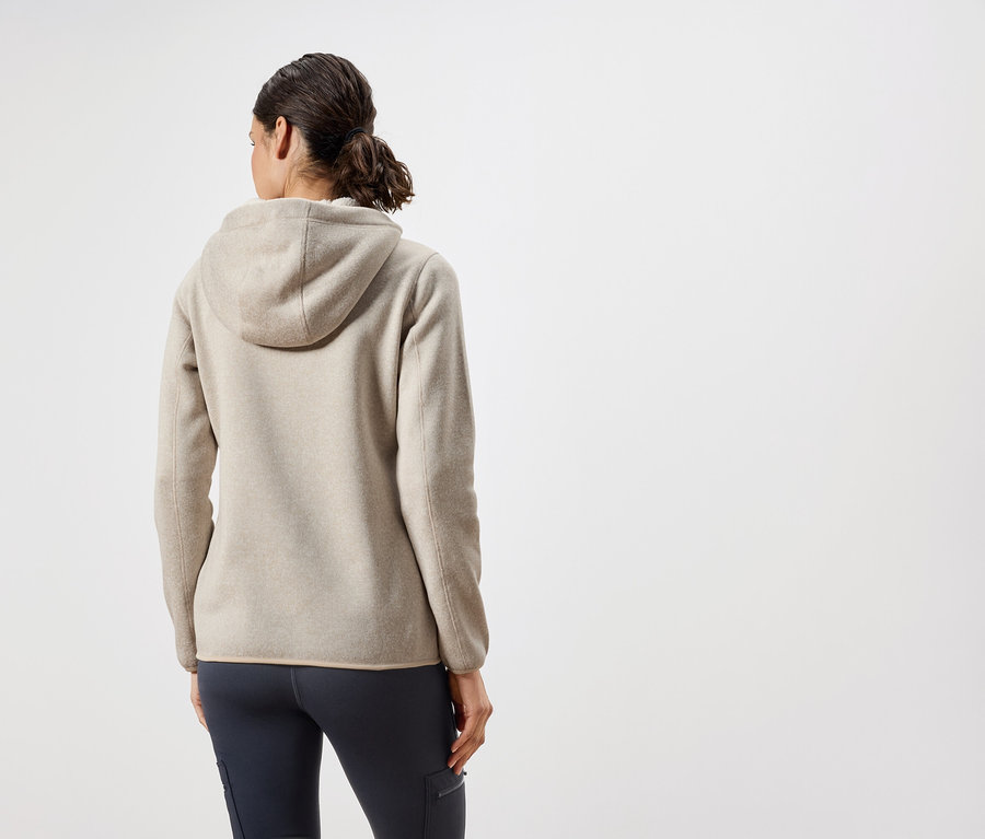 Von hinten ist eine Frau in einer beigen Kapuzenjacke und dunkelblauen Hosen zu sehen.