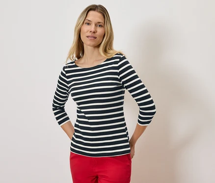 Blonde Frau trägt ein gestreiftes Dreiviertelarmshirt und rote Hosen.
