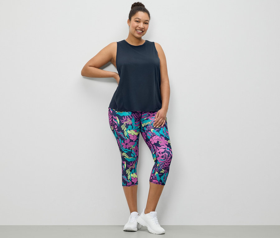 Frau posiert in einem dunkelblauen Sport-Top und einer 3/4-Sporttight mit Alloverprint.