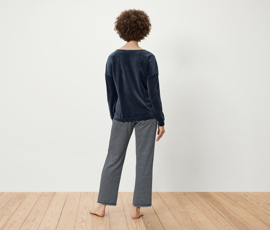 Frau mit lockigem Haar steht mit dem Rücken zur Kamera und trägt ein marineblaues Samtoberteil und eine gestreifte Hose.