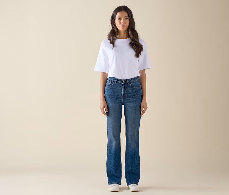 Eine Frau steht und trägt ein weißes T-Shirt, blaue Jeans und weiße Turnschuhe.