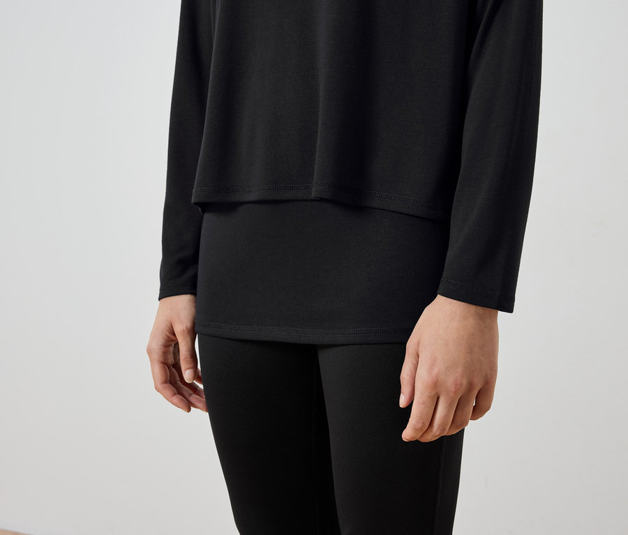 Oberkörper einer Person, die ein schwarzes Langarmshirt und eine schwarze Leggings trägt.