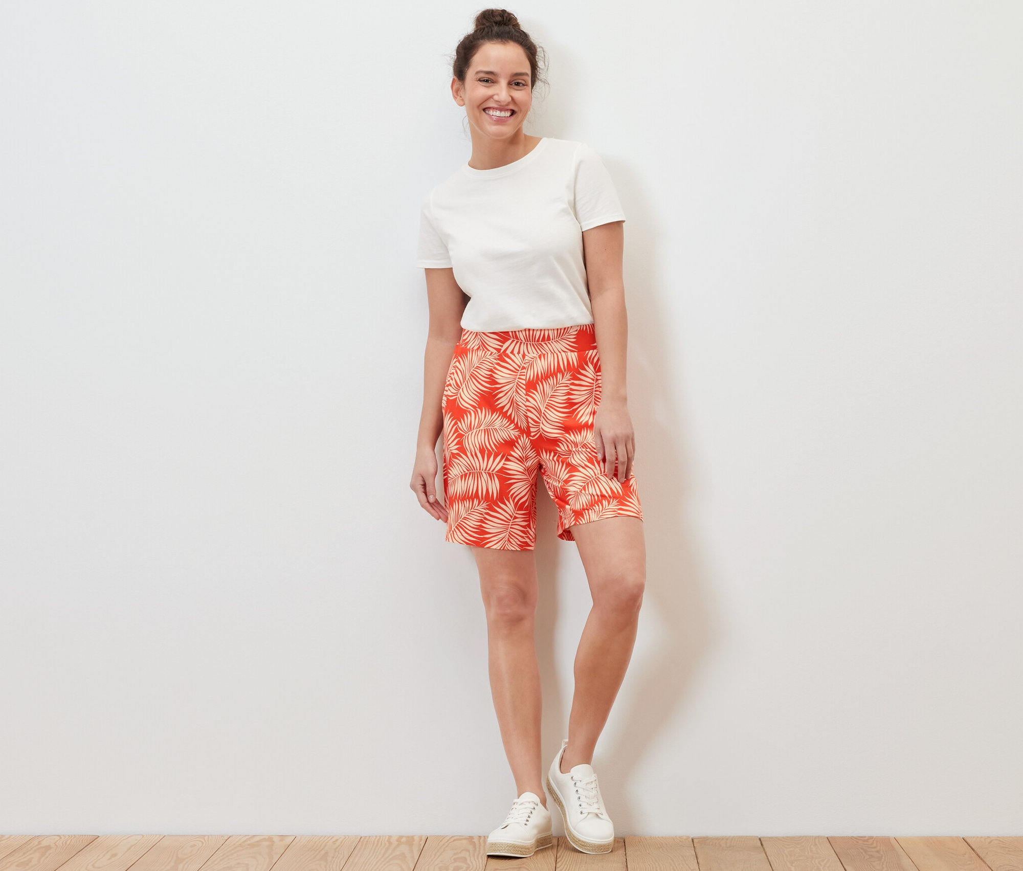 Eine Frau steht und trägt bedruckte Jerseyshorts und ein weißes T-Shirt.