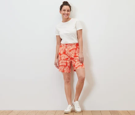 Eine Frau steht und trägt bedruckte Jerseyshorts und ein weißes T-Shirt.