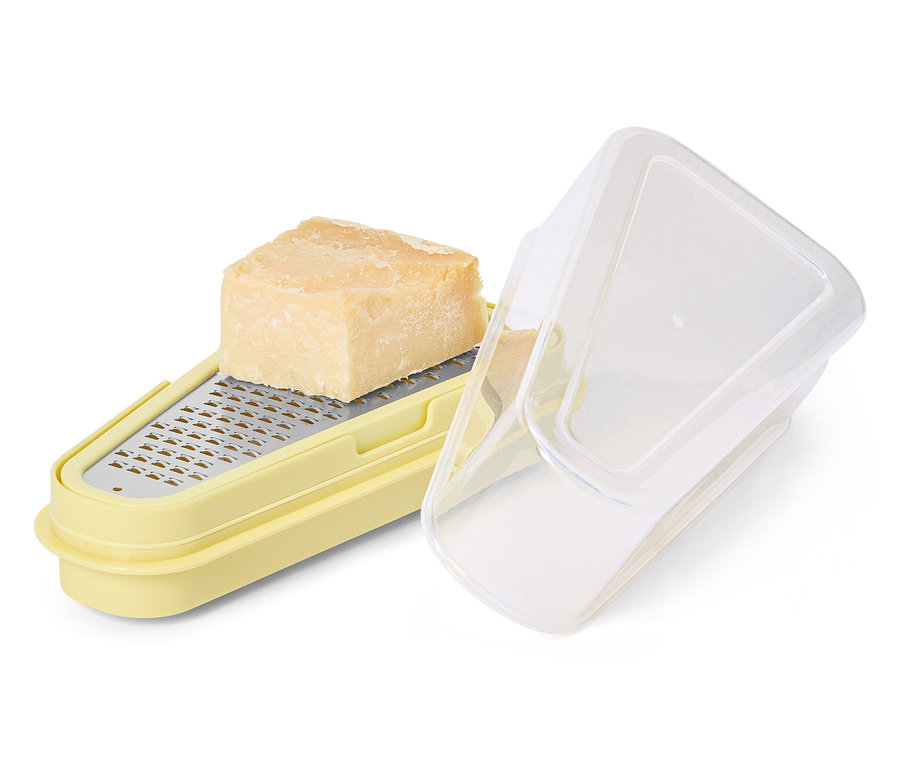 Parmesan liegt auf gelber Parmesanreibe mit Behälter.