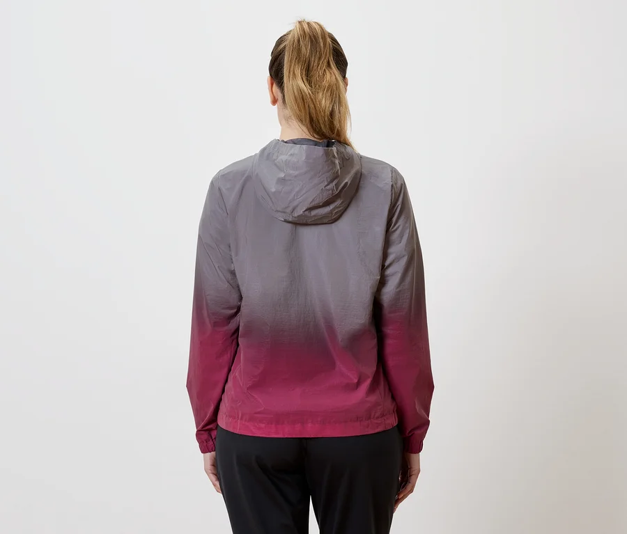 Rückansicht einer Frau mit Pferdeschwanz, die eine Kapuzenjacke mit Farbverlauf von Grau nach Pink und eine schwarze Hose trägt.