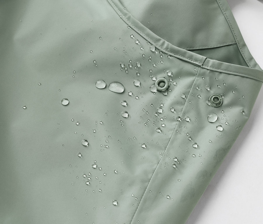 Nahaufnahme eines wasserabweisenden, hellgrünen Stoffes mit Wassertropfen und zwei Druckknöpfen.