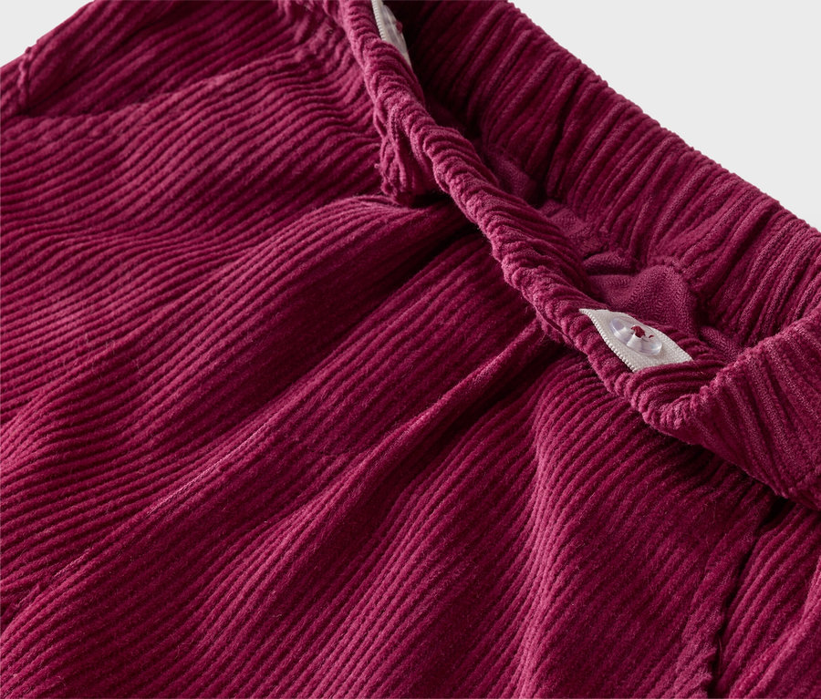Nahaufnahme einer weinroten Kordhose mit elastischem Bund und Knopfverschluss.