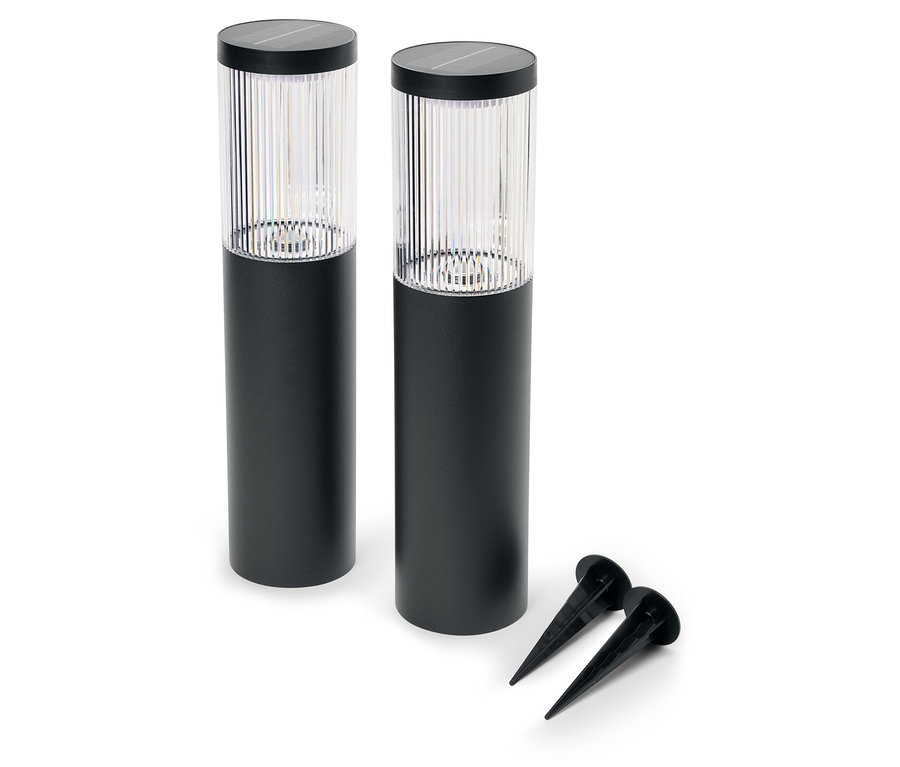 Zwei schwarze Gartenleuchten und zwei Erdspieße liegen auf einem weißen Hintergrund.