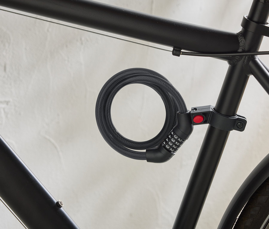 Ein schwarzes Fahrrad ist mit einem spiralförmigen Kabelschloss mit Zahlencode am Rahmen befestigt.