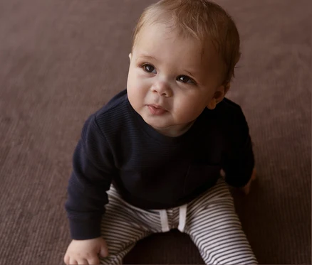 Baby sitzt auf dem Boden und trägt eine NAME IT Baby-Jerseyhose mit Streifen.