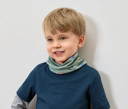 Lächelnder Junge mit blonden Haaren und blauem T-Shirt trägt einen grünen Schal mit Tiermuster.