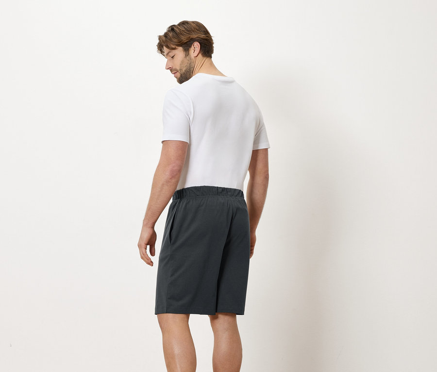 Mann von hinten in einem weißen T-Shirt und grauen Shorts vor einem weißen Hintergrund.